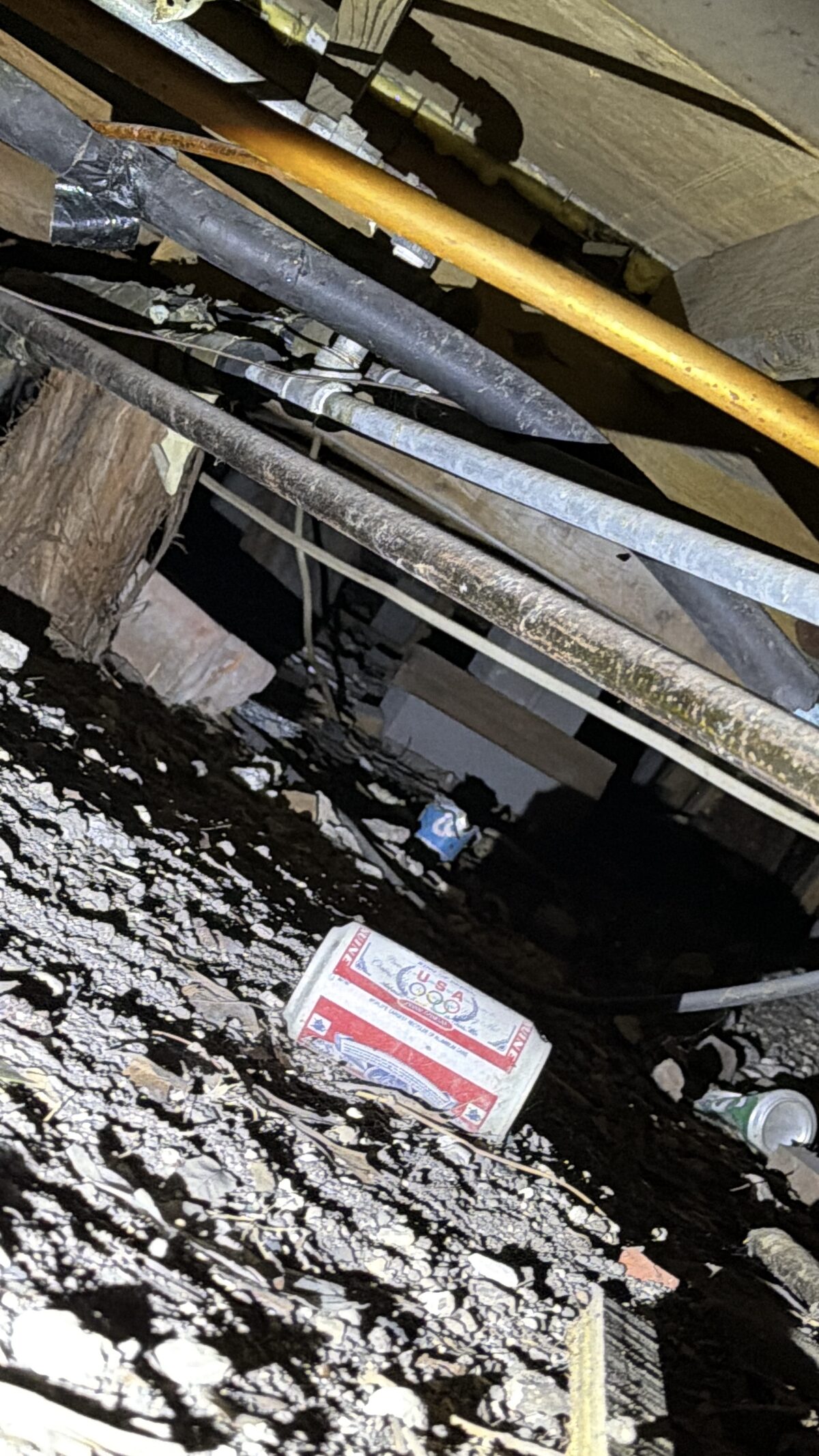 Faded vintage drink cans resting on rocky crawlspace soil beneath old pipes