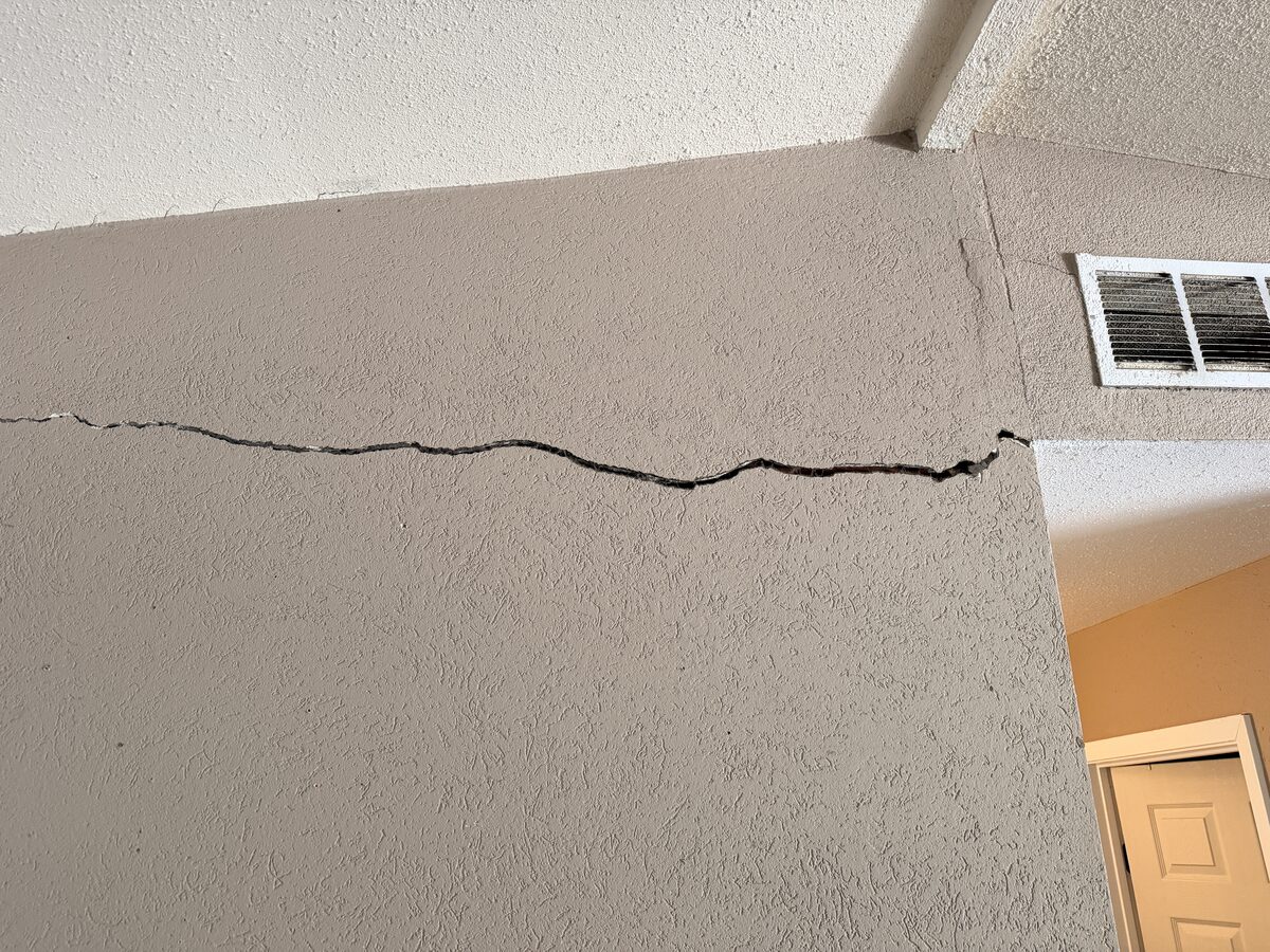 Wide horizontal crack across a textured wall below a ceiling vent