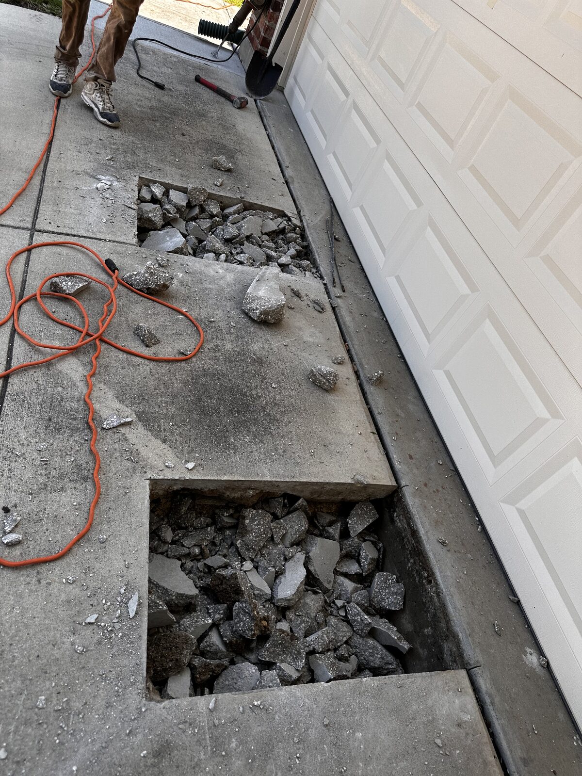Open pier hole at the edge of a slab foundation with a digging bar, ready for steel pier installation