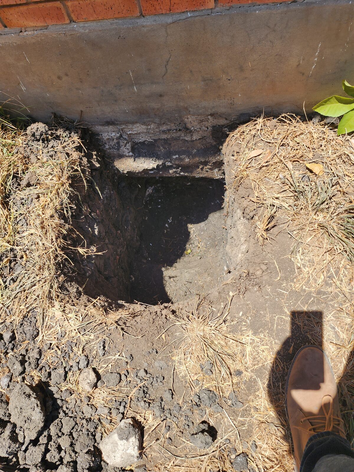 Open pier pits dug along the foundation line of a brick home during underpinning work