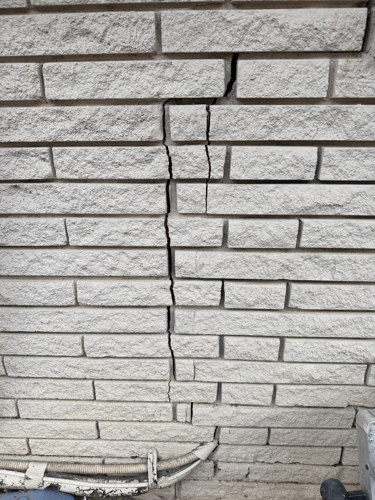 Open vertical crack splitting a stone veneer wall, severe evidence of foundation settlement