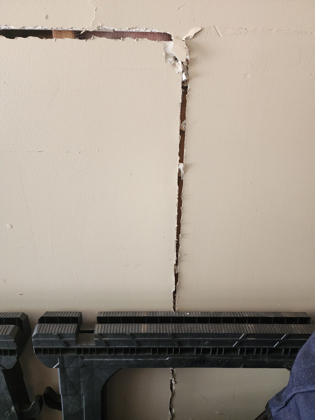 Vertical drywall crack with peeling joint tape and corner separation caused by foundation movement
