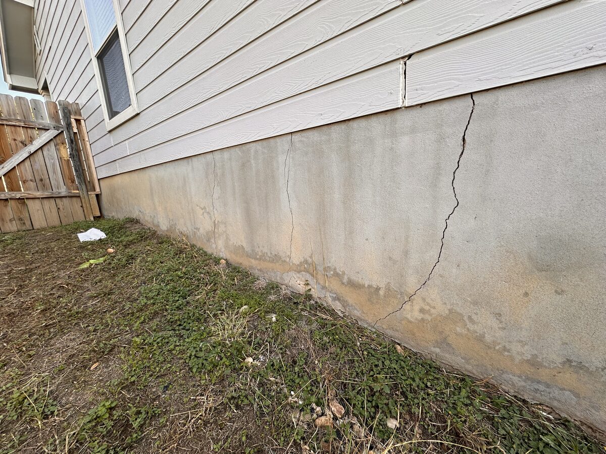 Side view of a perimeter stem wall with a visible settlement crack along a fenced side yard
