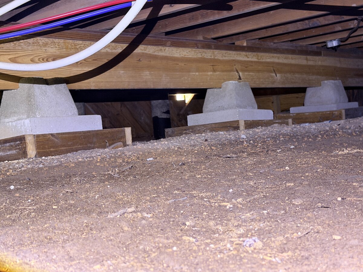 Tapered concrete pier block set on wood boards directly on crawl space soil
