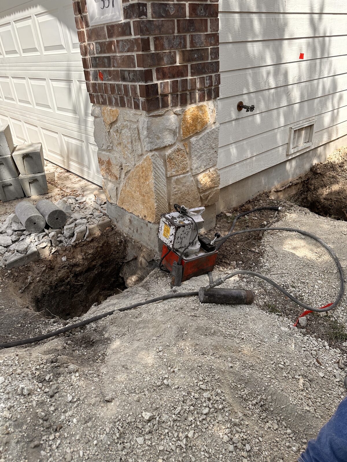Hydraulic pier-driving ram set in an excavated pit at a brick corner during house leveling