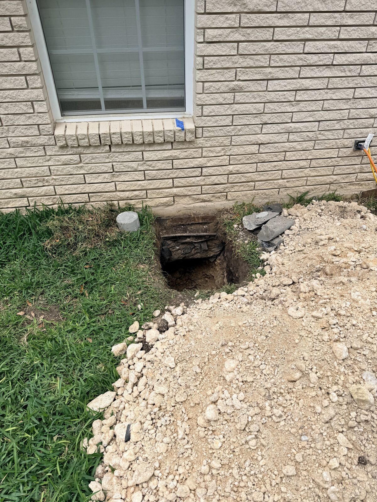 Pier hole and excavated caliche soil beneath a window during foundation repair on a brick home