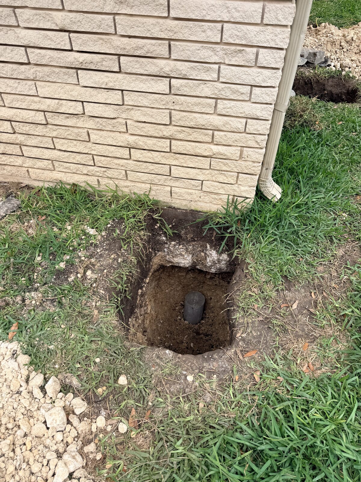 Pier hole excavated at a home's corner near the downspout to stabilize a settling foundation