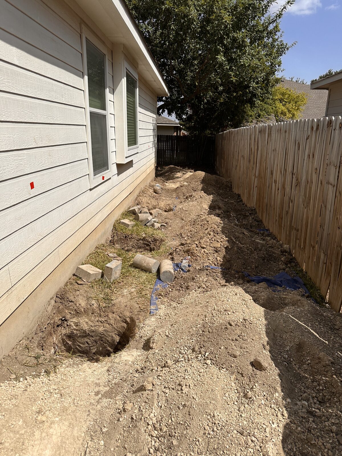 Row of pier holes dug along a foundation in the narrow side yard between a home and privacy fence