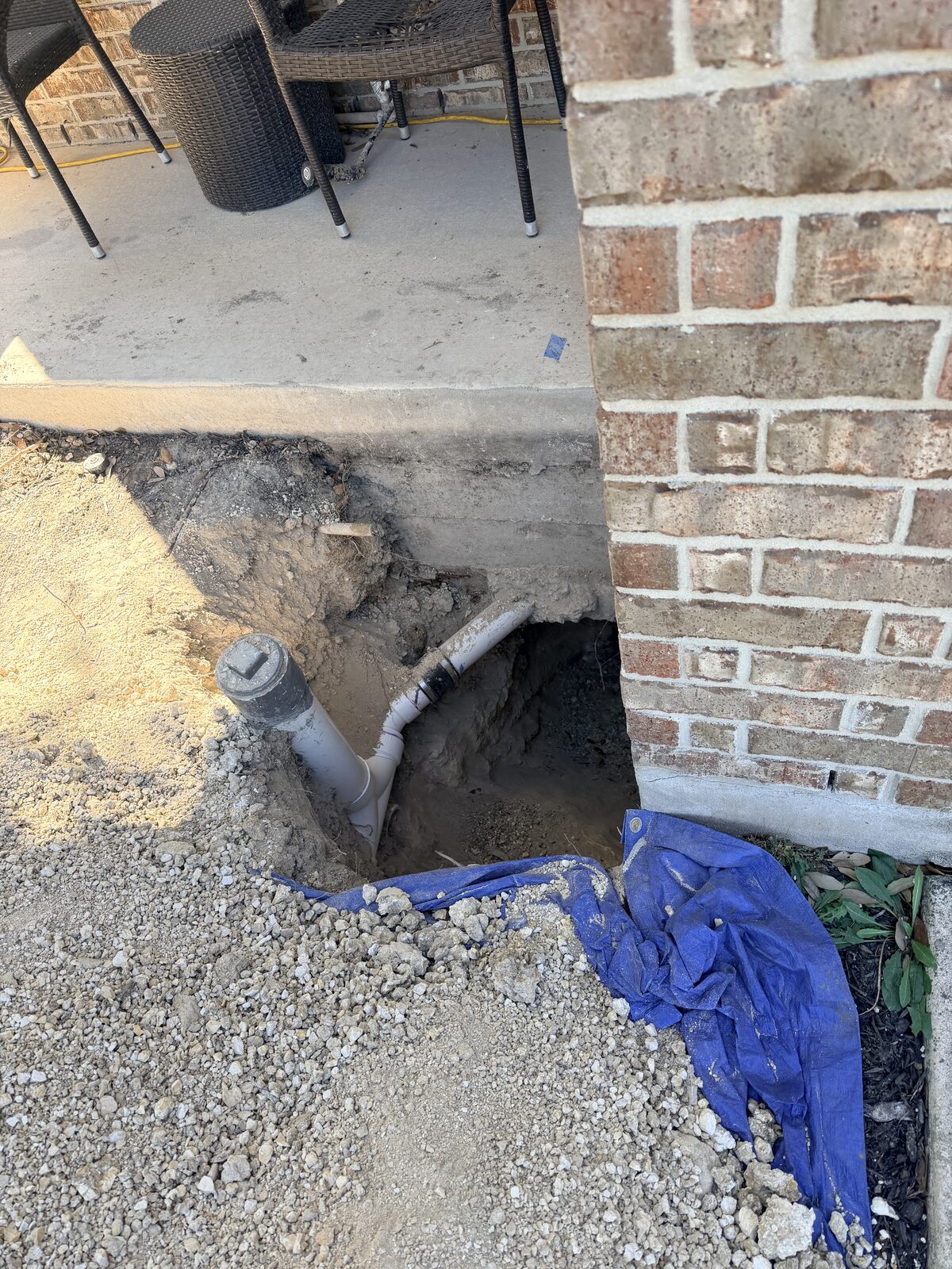 Pier pit excavation exposing a drain line beneath a brick home