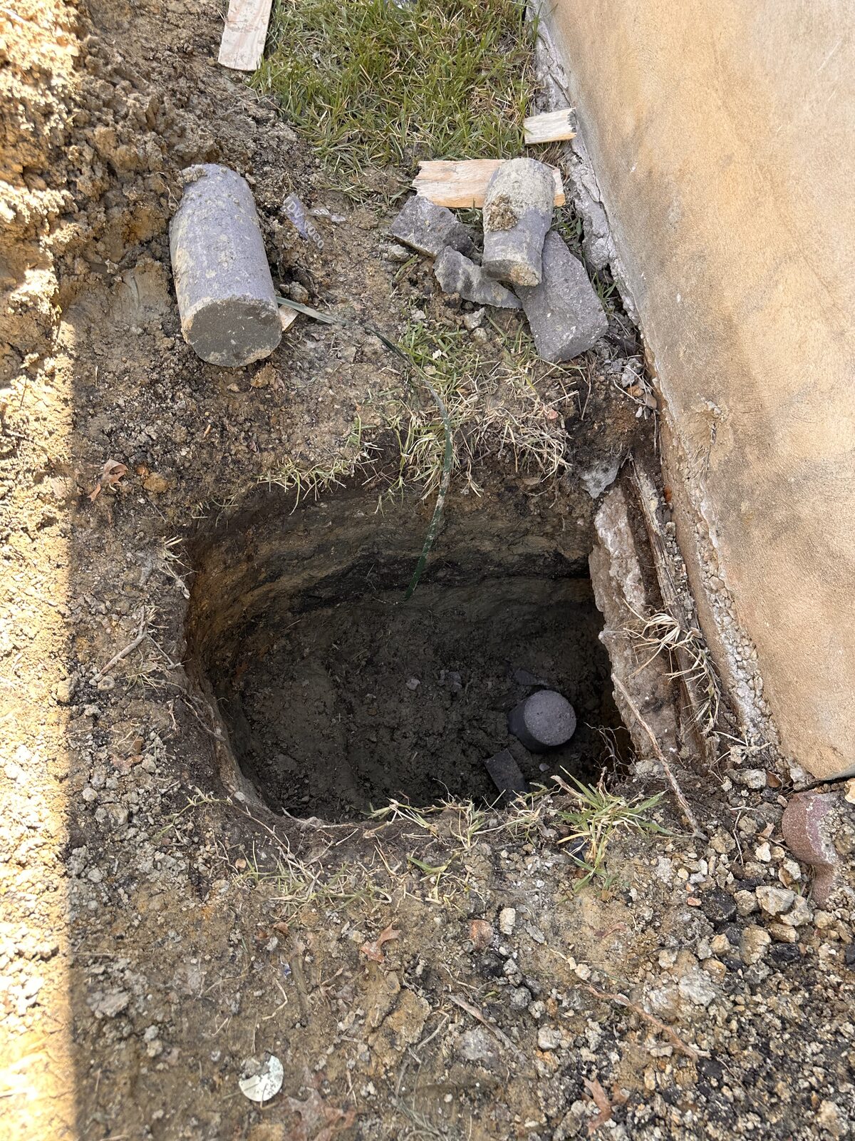 Open pier pit beside a stem wall with concrete piling segments staged for pressing beneath the foundation
