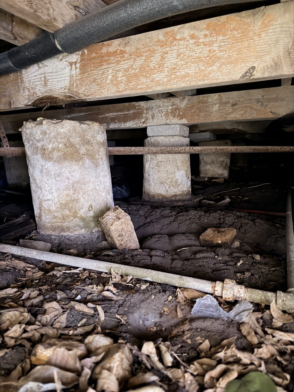 Shimmed concrete pier supporting wood beams in the crawl space of a pier and beam house