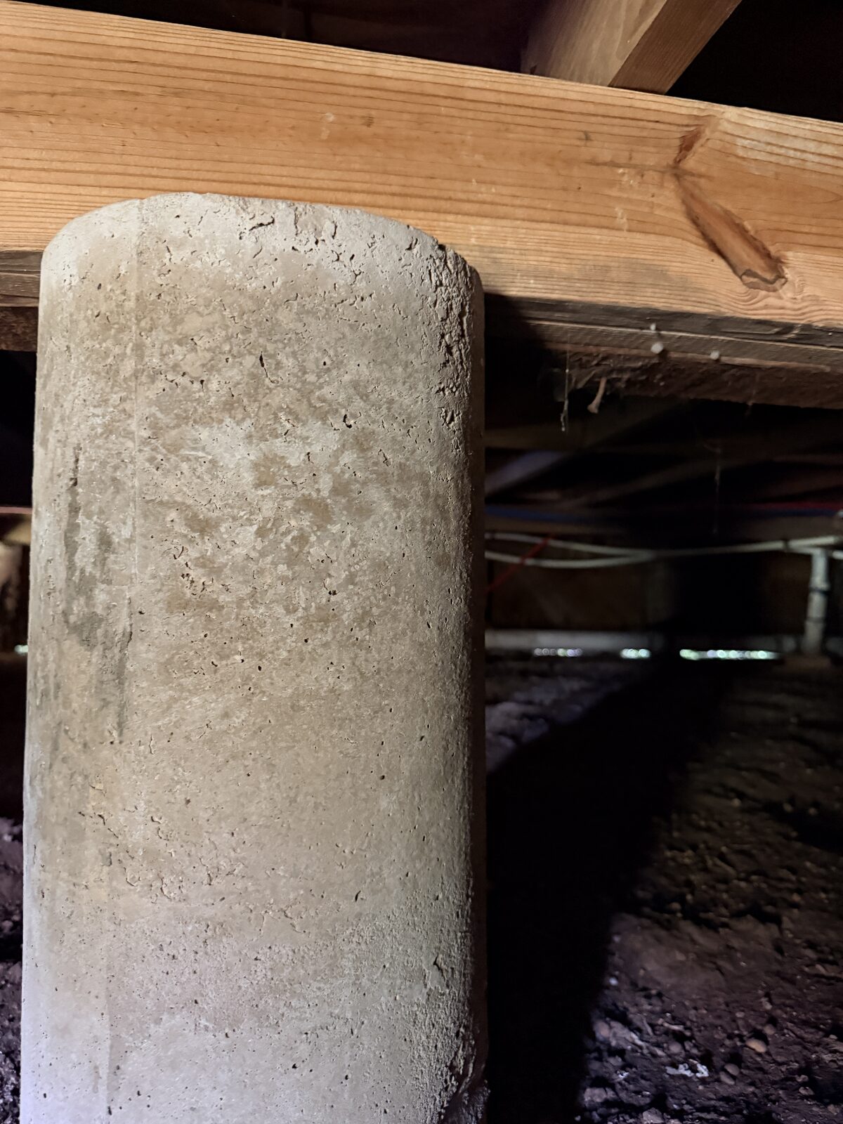 Close view of a wood beam bearing on a concrete pier in a crawl space