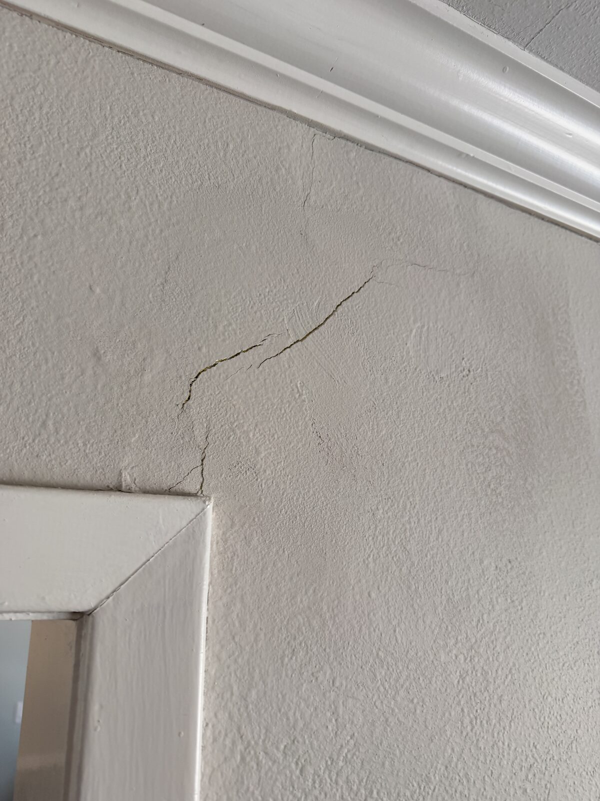Cracked plaster above an interior door trim in an older home, a sign of foundation movement
