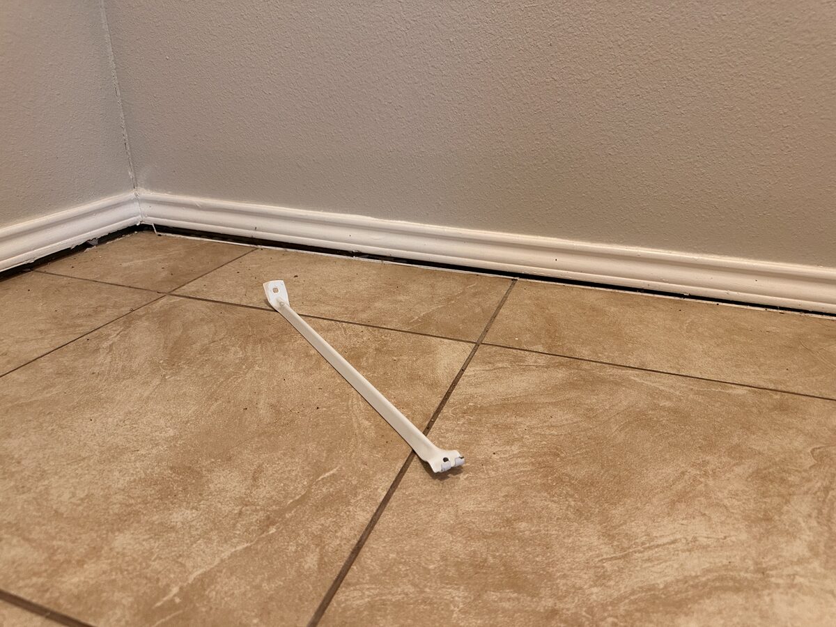 Piece of trim popped off and lying on the tile floor after baseboard separation in a settling home