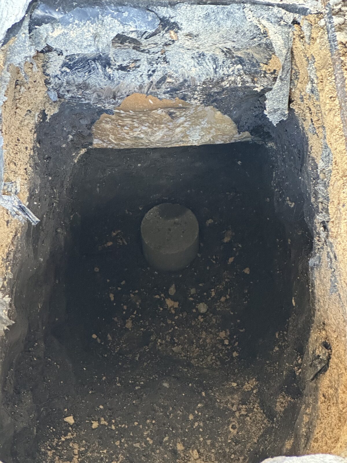 Deep excavation pit showing a pressed concrete pile segment beneath a home's foundation