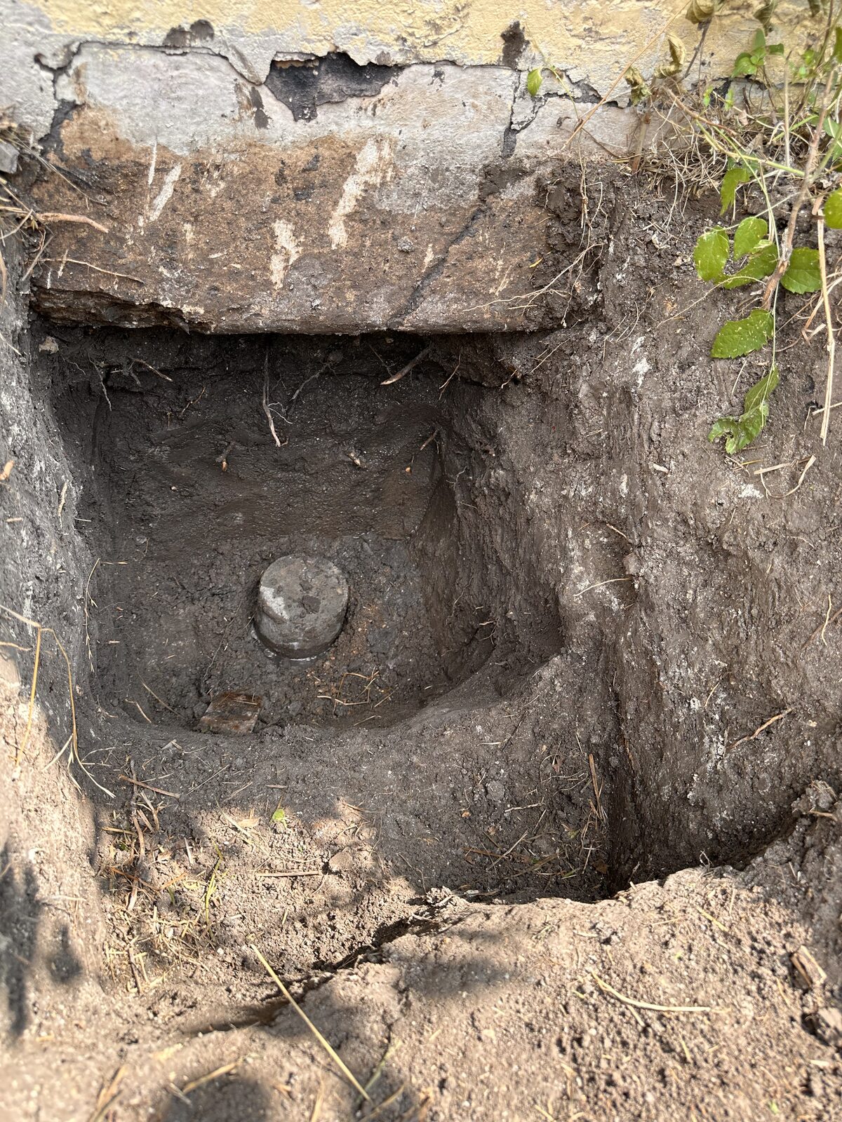 Round head of a pressed concrete pile at the bottom of a pier pit beneath a home's grade beam