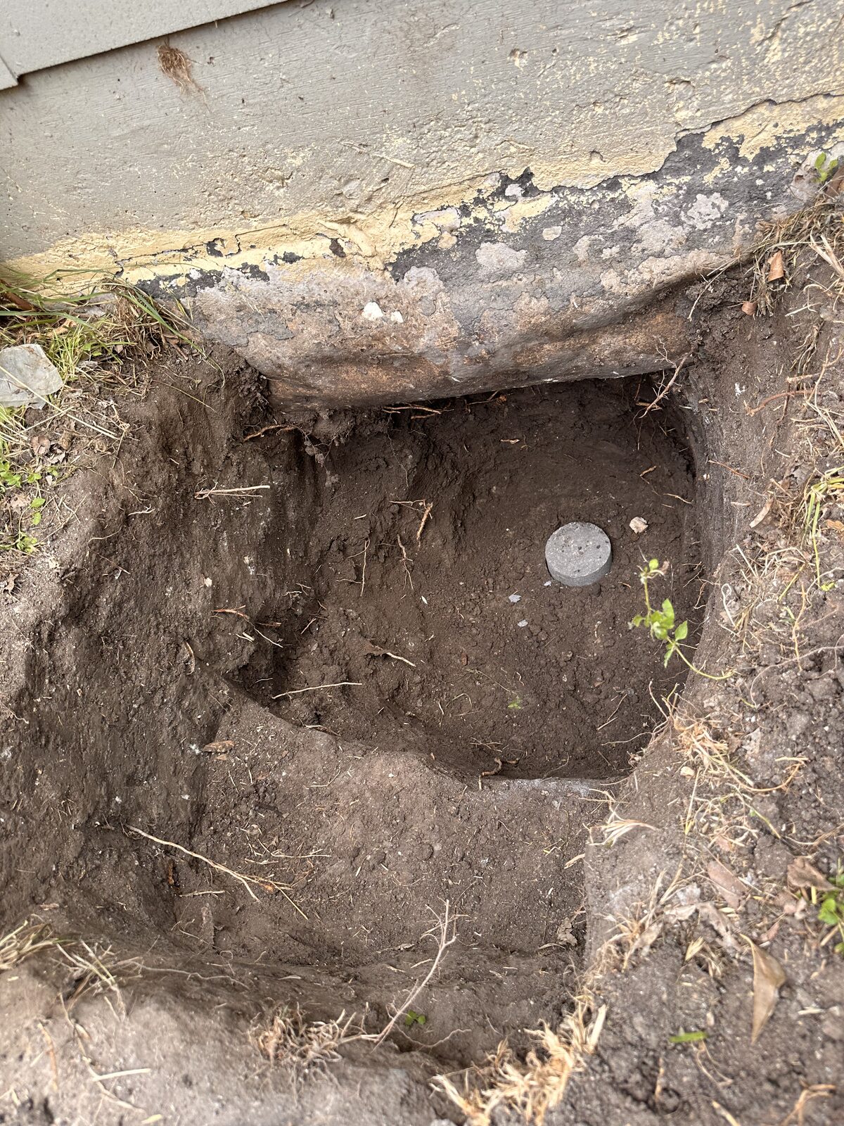 Pressed concrete pile installed in a pit beneath the wood-sided wall of a pier-and-beam home