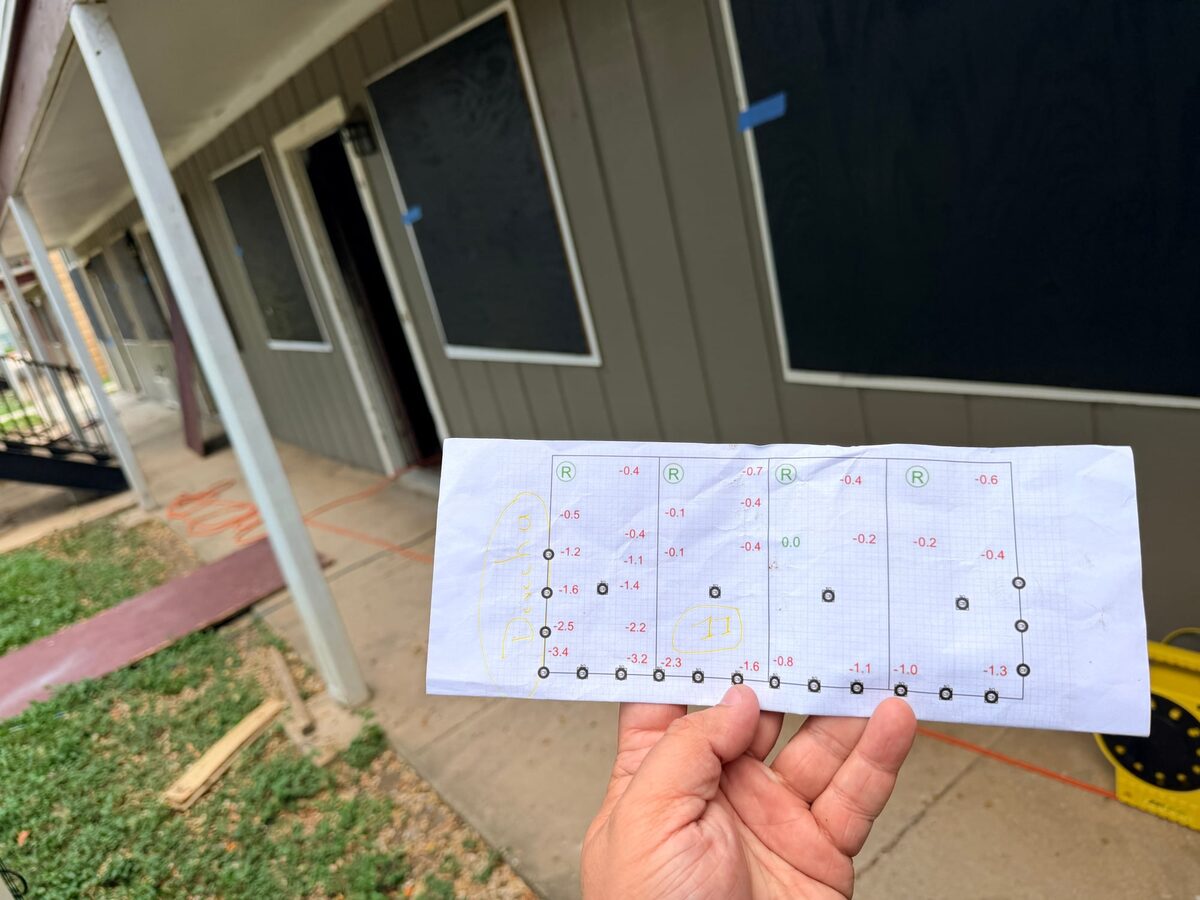 Printed pier plan showing elevation readings and marked pier spots, held up in front of an apartment building