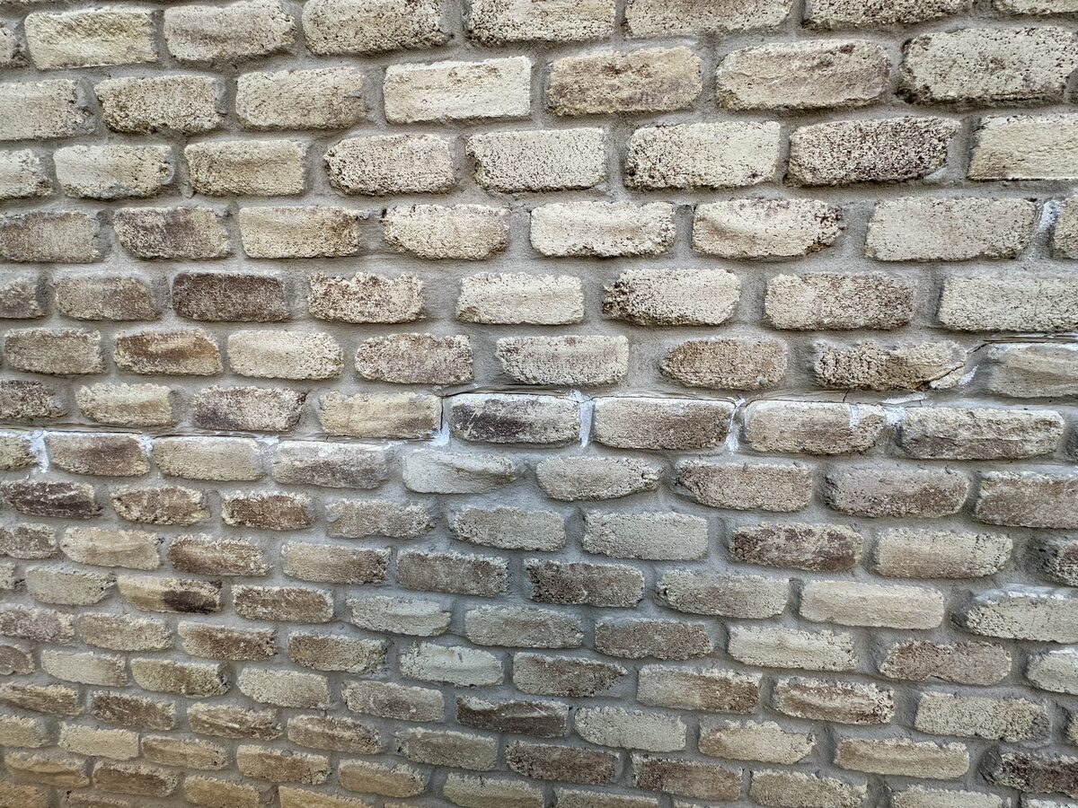 Patched and repointed mortar joints in a tan brick wall, evidence of previous foundation-related cracking