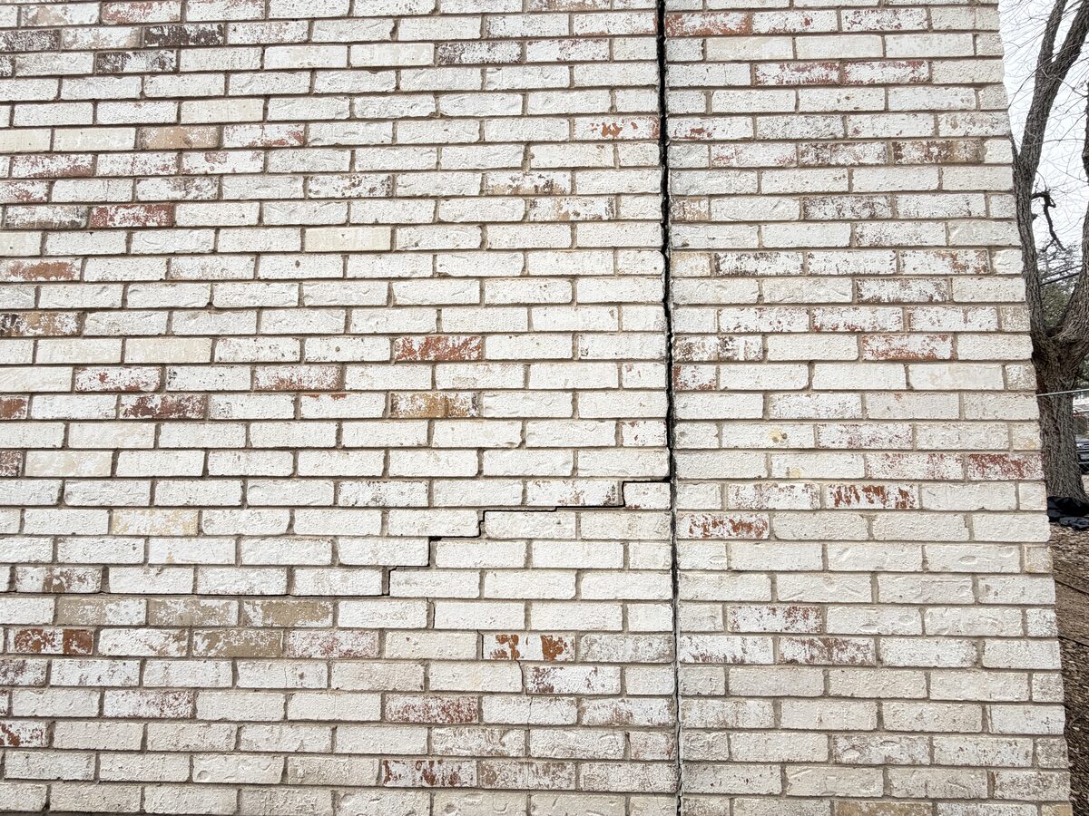 Painted brick wall with a repointed vertical crack line, repaired after foundation settlement