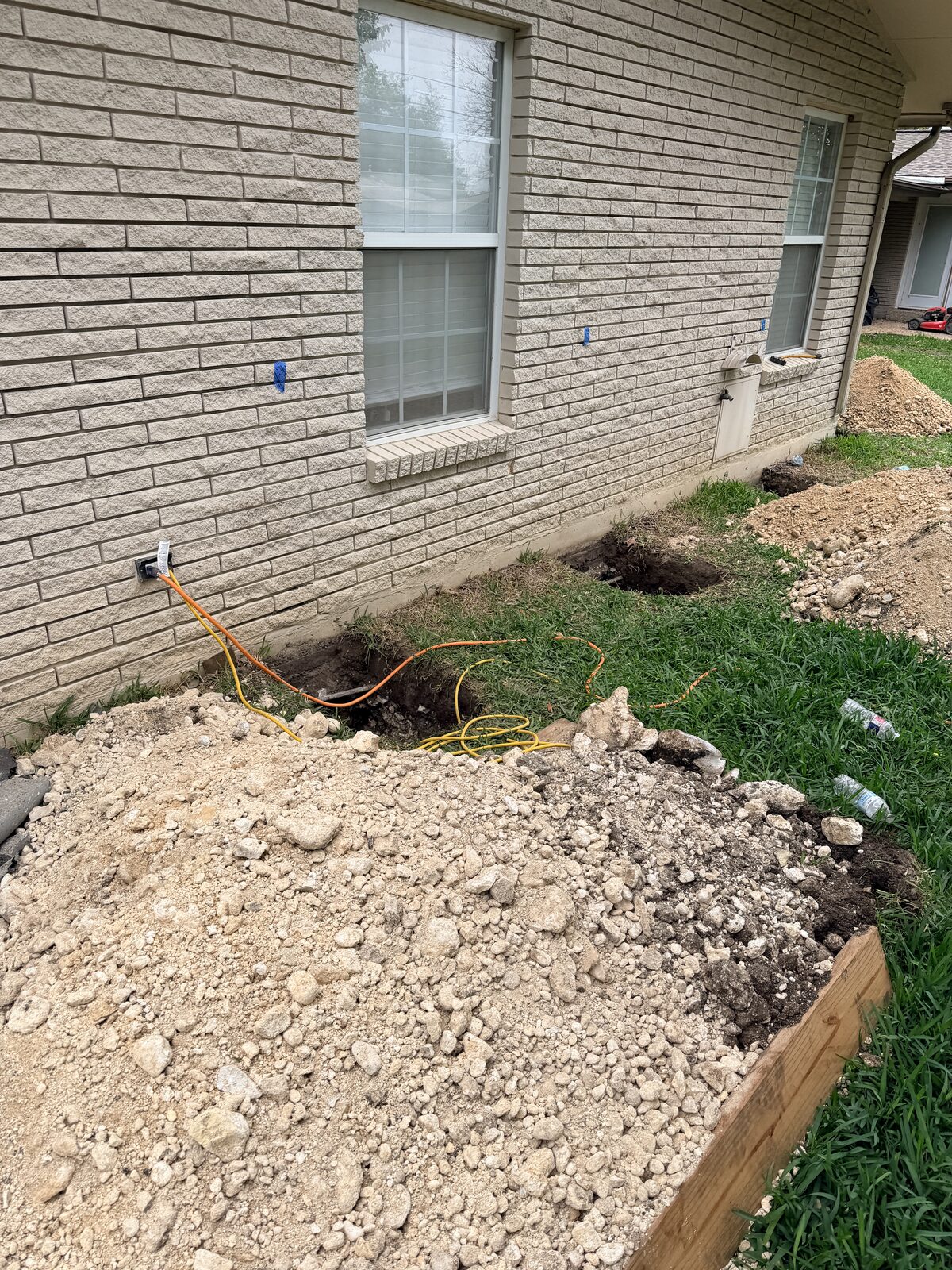 Row of pier holes excavated along a brick home's foundation in preparation for steel pier installation