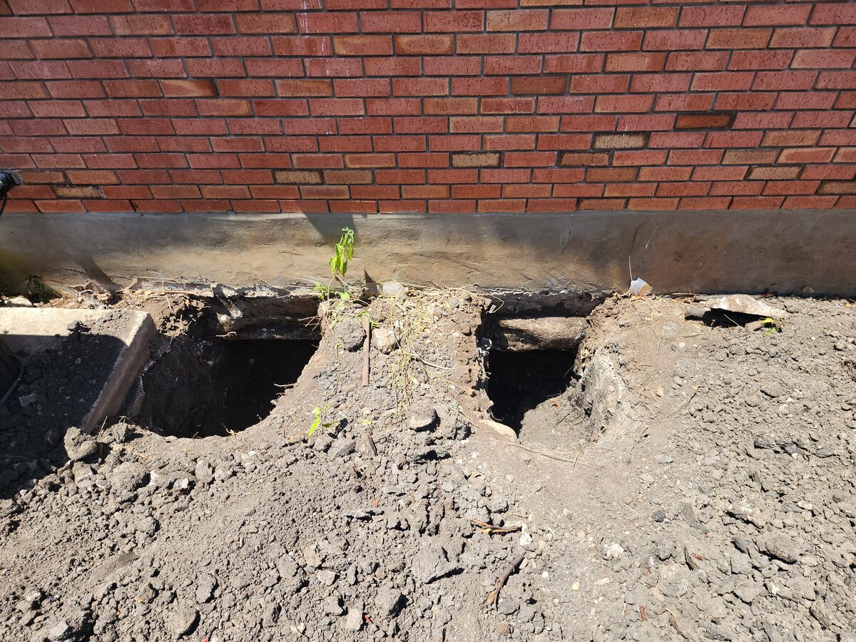 A row of hand-dug pier pits spaced along a home's foundation during pier installation