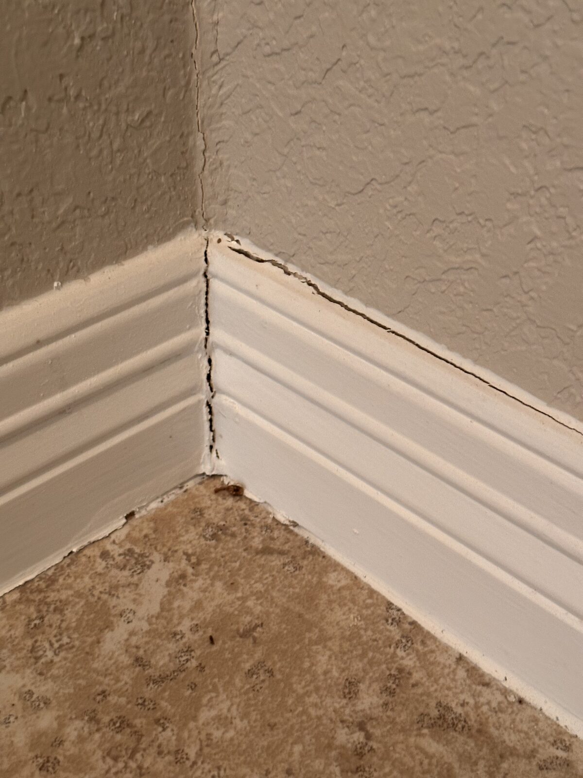 Separated baseboard joint and corner crack above a tile floor inside a settling home