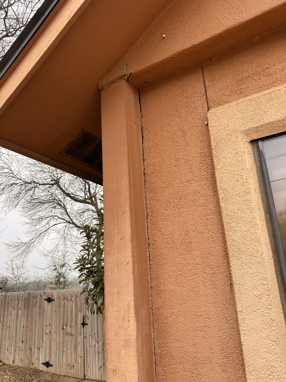 Separation gap opening at the top corner of an exterior door frame, an early sign of foundation settlement