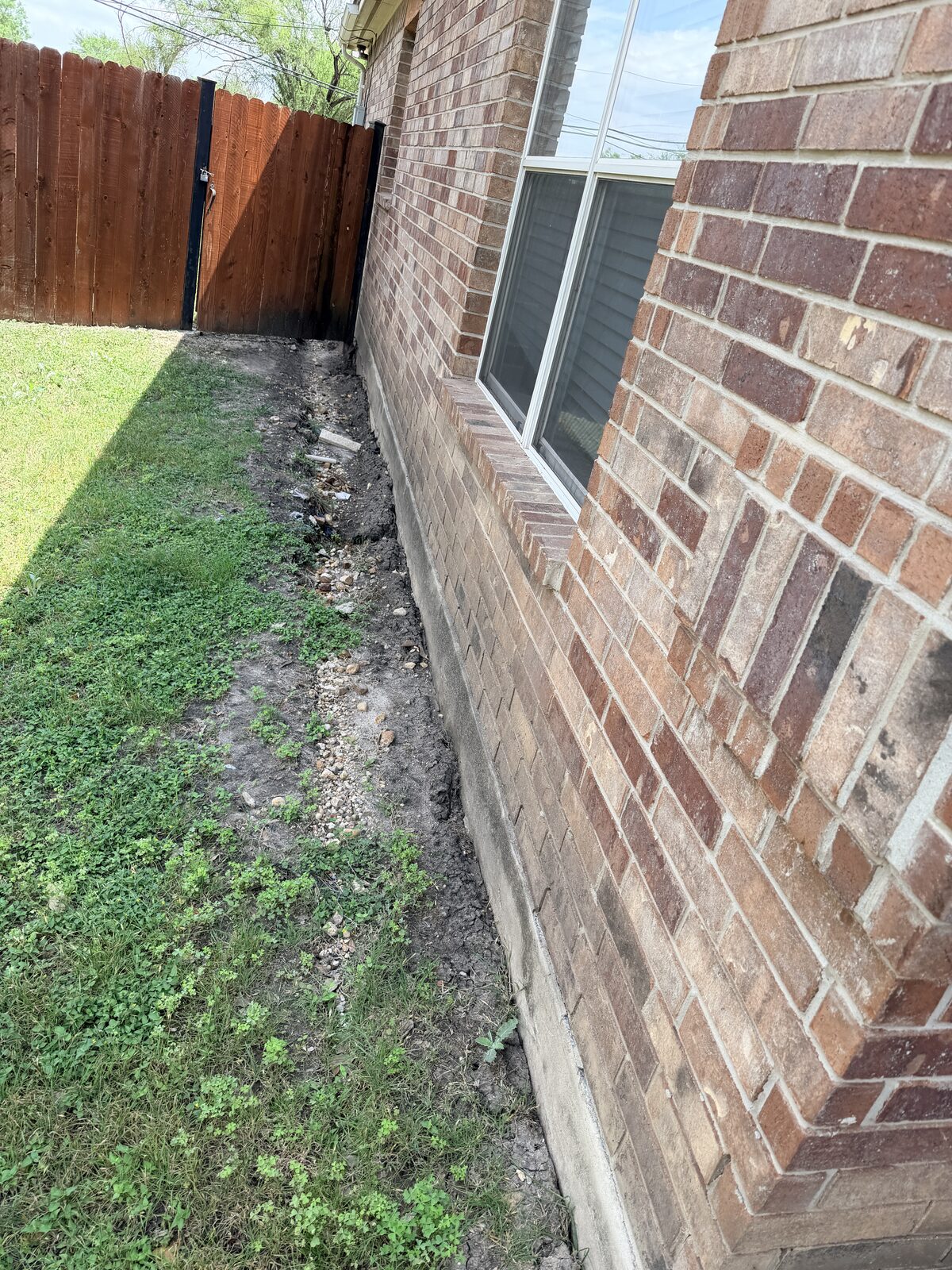 Settled and pulled-away soil along the brick veneer foundation of a Central Texas home