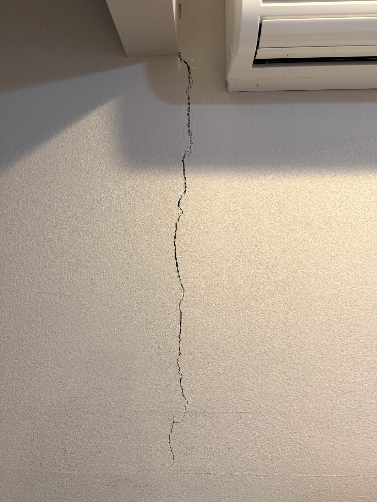 Settlement crack in drywall below a ceiling beam beside a mini-split unit before foundation repair