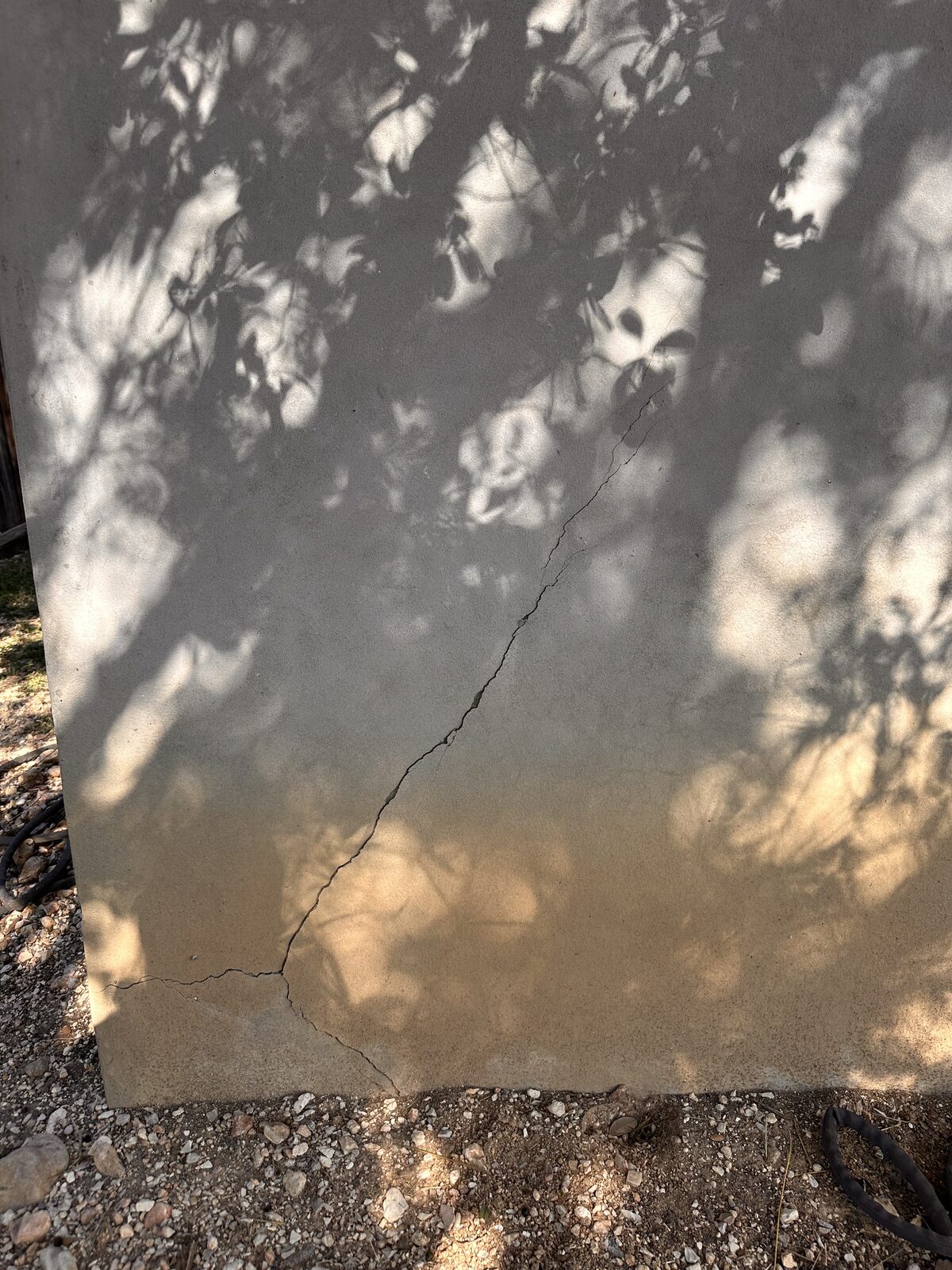 Settlement crack across a shaded corner of a concrete perimeter wall at grade
