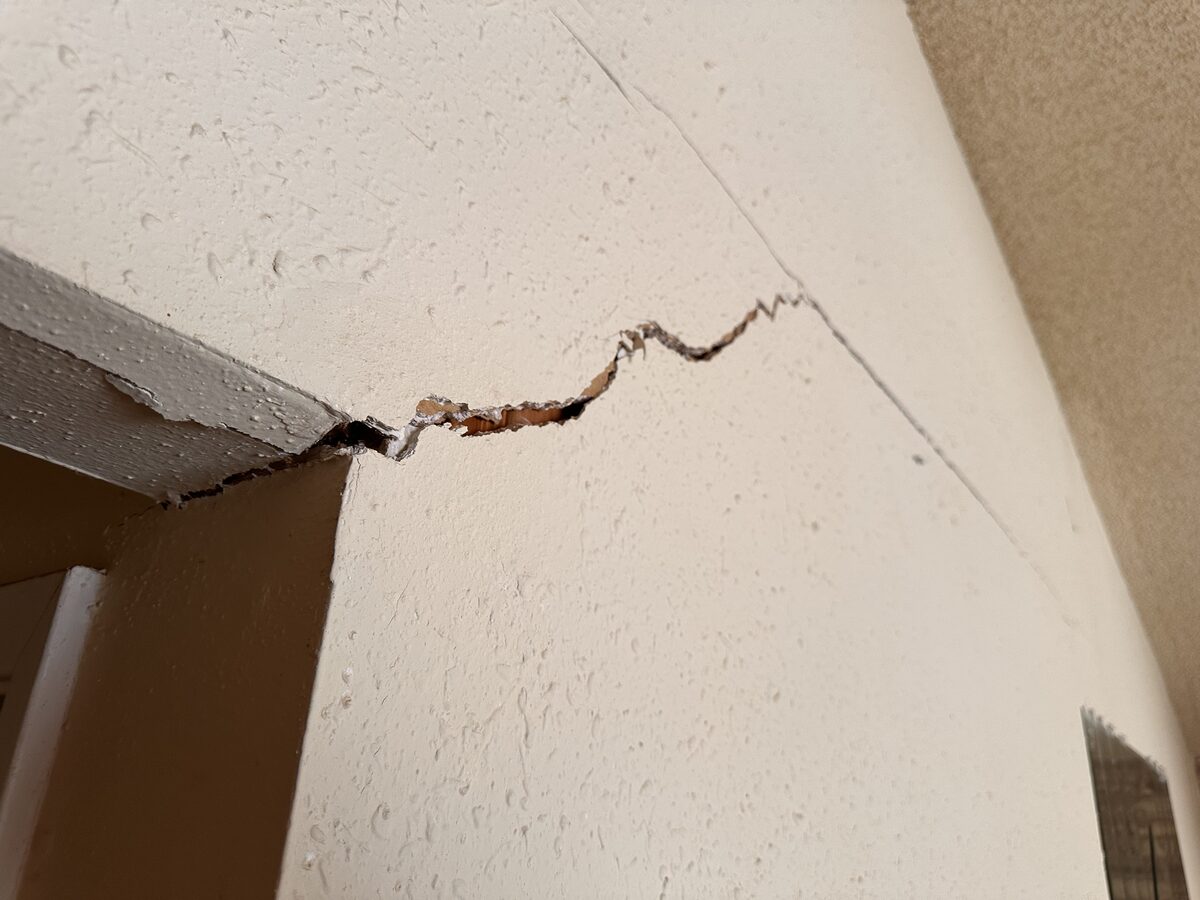Severe zigzag separation crack with flaking plaster at the ceiling line of a settling home
