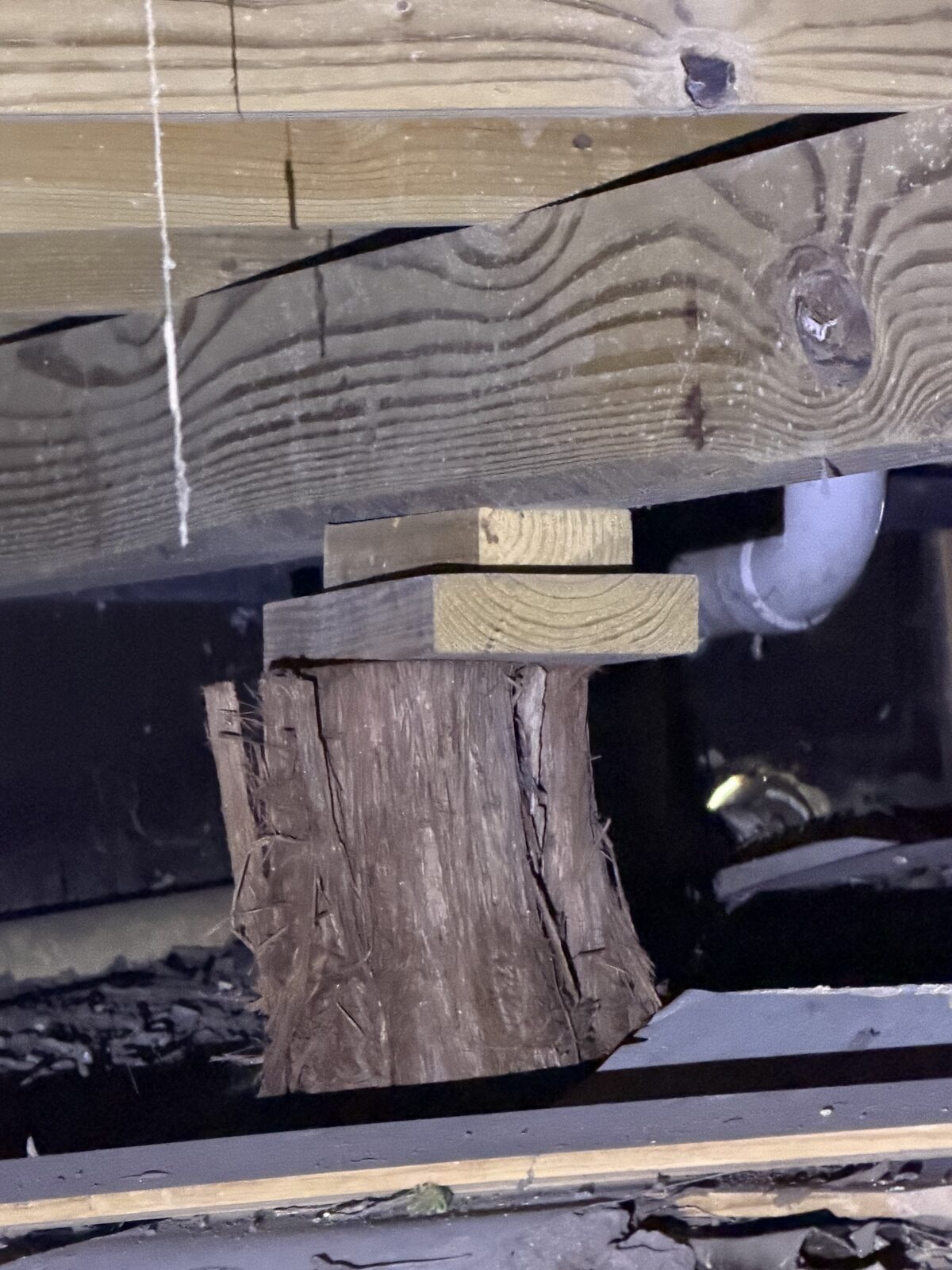 Wood shim blocks stacked between a split cedar post and floor beam
