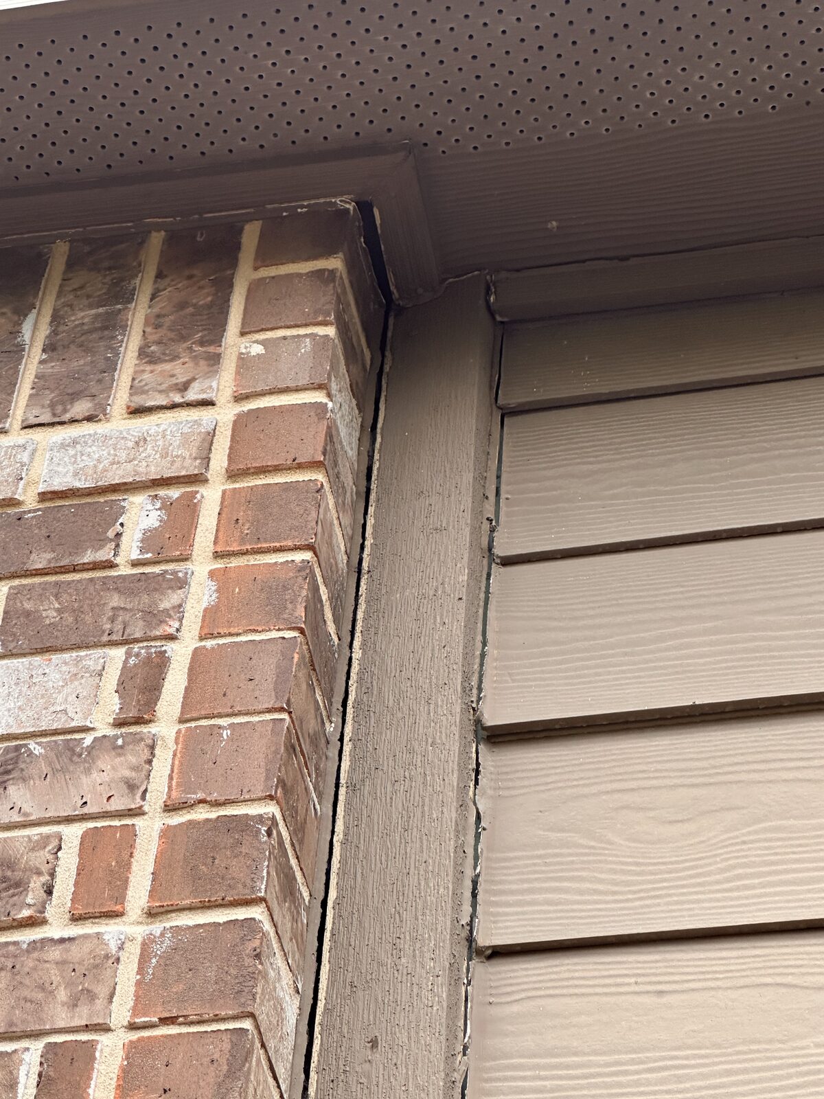 Separation at the soffit trim where a brick column meets siding, caused by a settling foundation