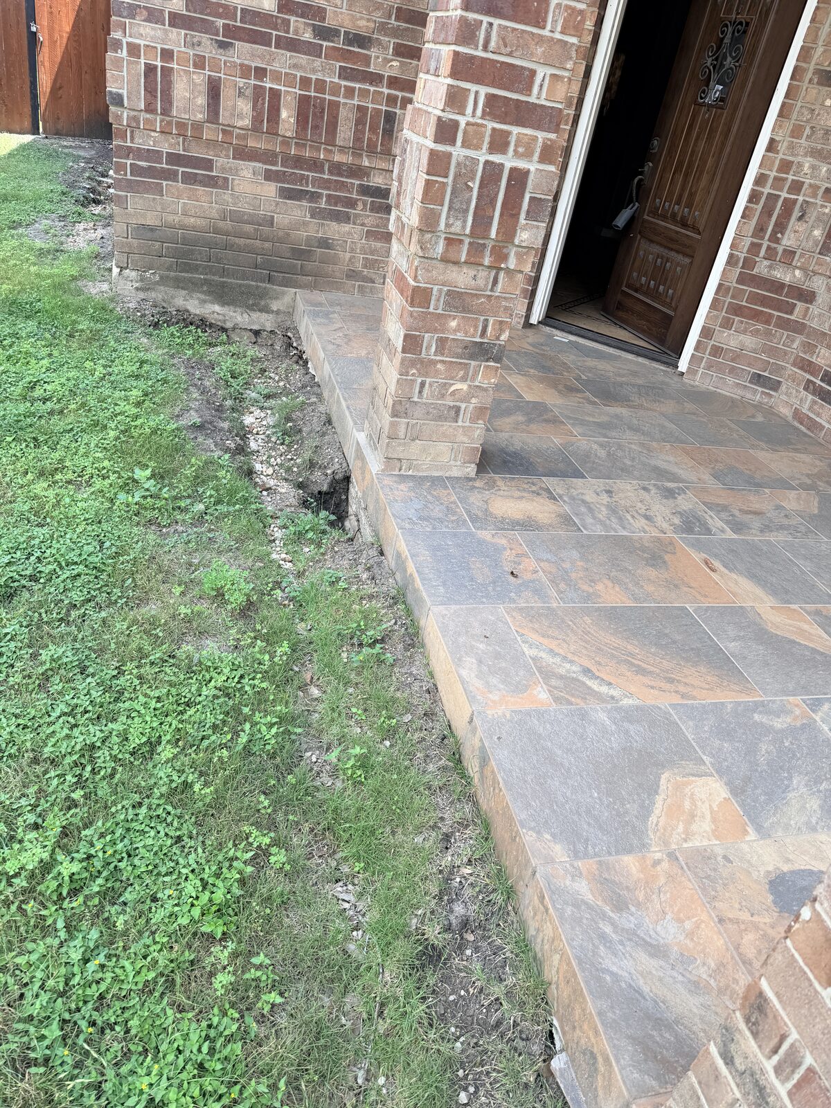 Soil settled away from a flagstone porch slab at a brick home entry, a common sign of foundation movement