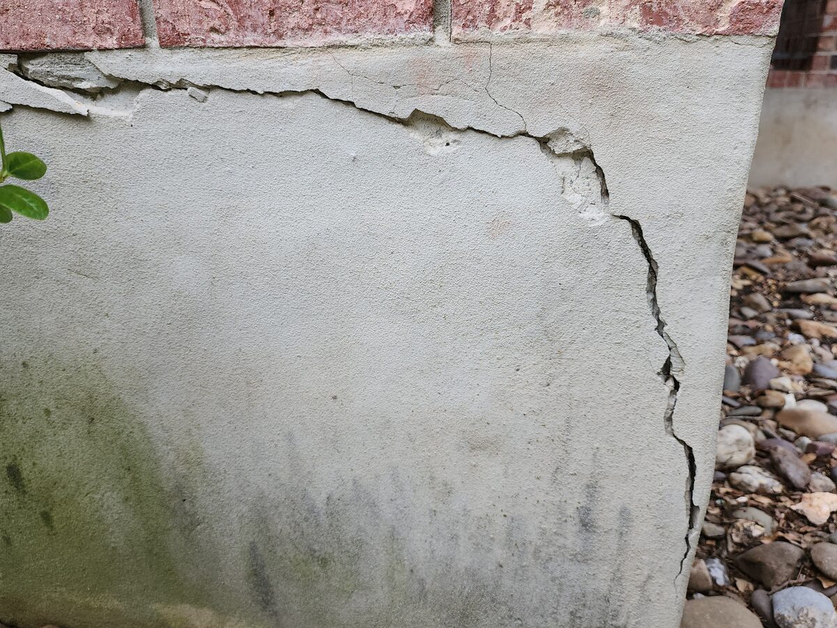 Spalled and cracked stucco at a foundation stem-wall corner beneath brick veneer, before foundation repair