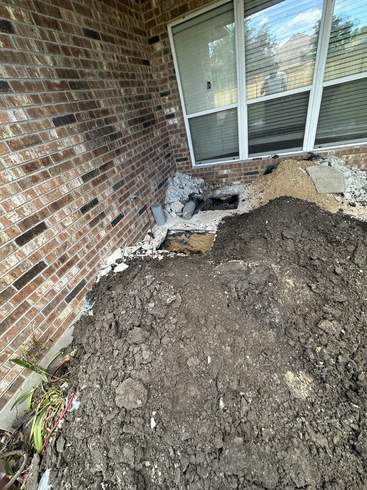 Excavated soil piled at a brick window corner where the foundation is exposed for pier installation