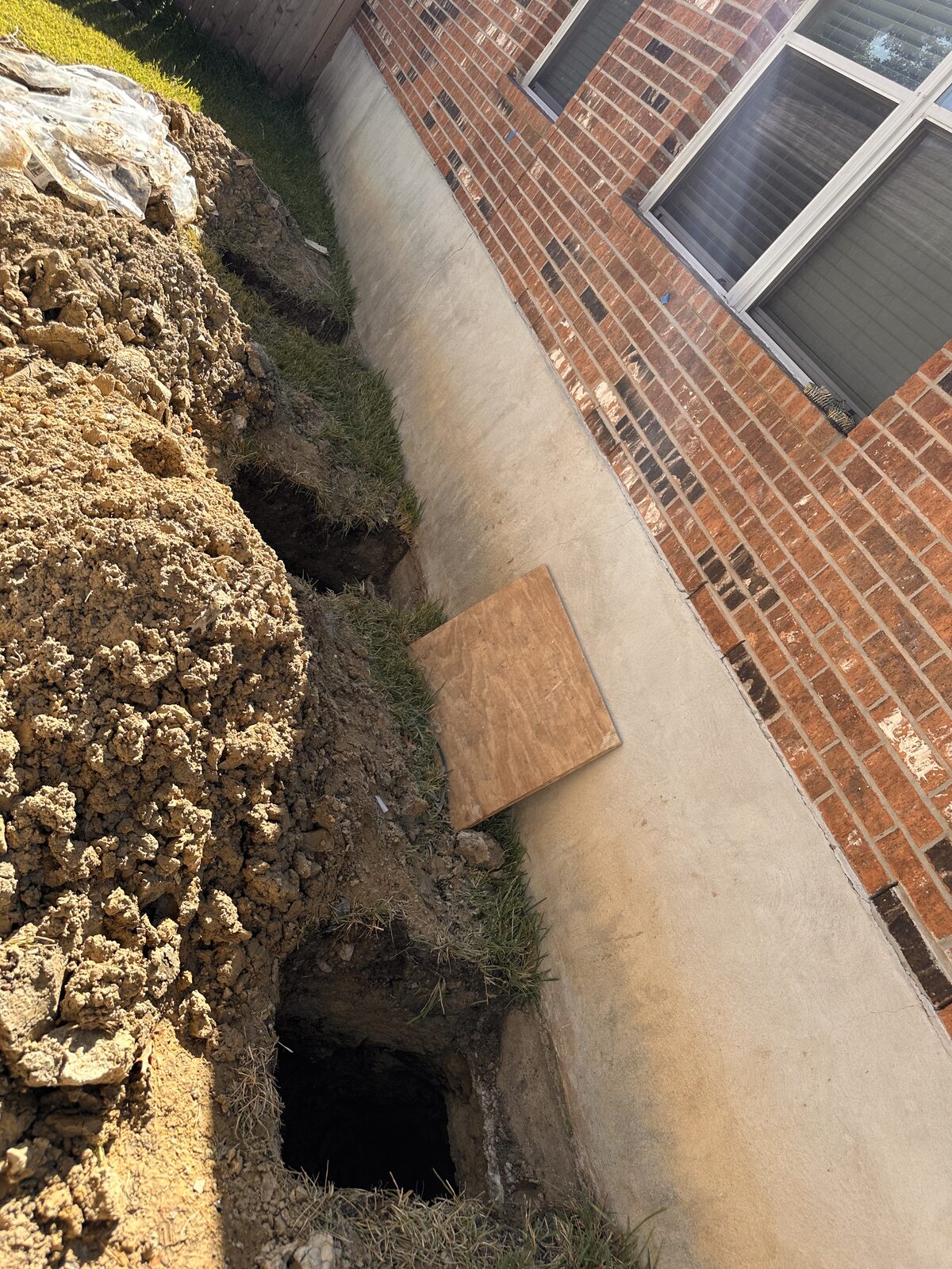 Spoil mound and open pier hole beneath a window along a home's foundation during underpinning