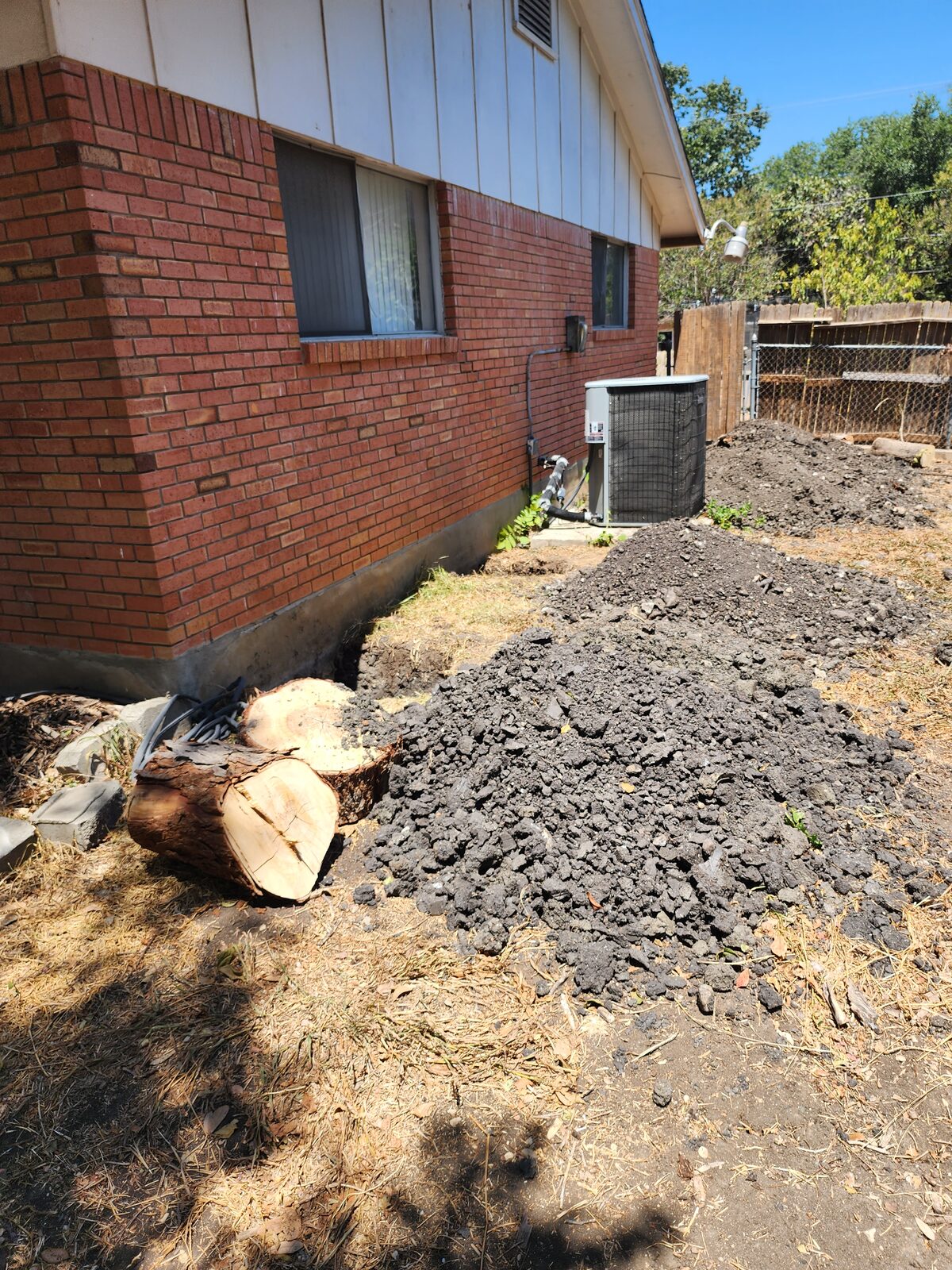 Excavated soil piled beside a home's exterior wall during foundation pier installation
