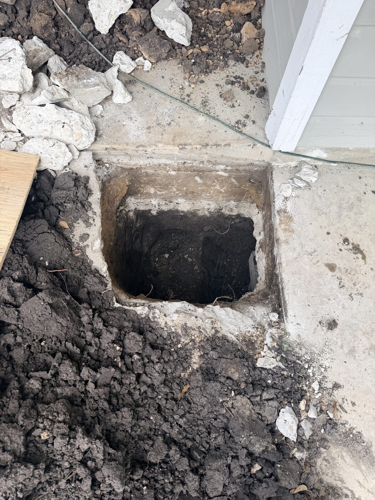 Square pier pit dug at a slab foundation edge with broken concrete removed