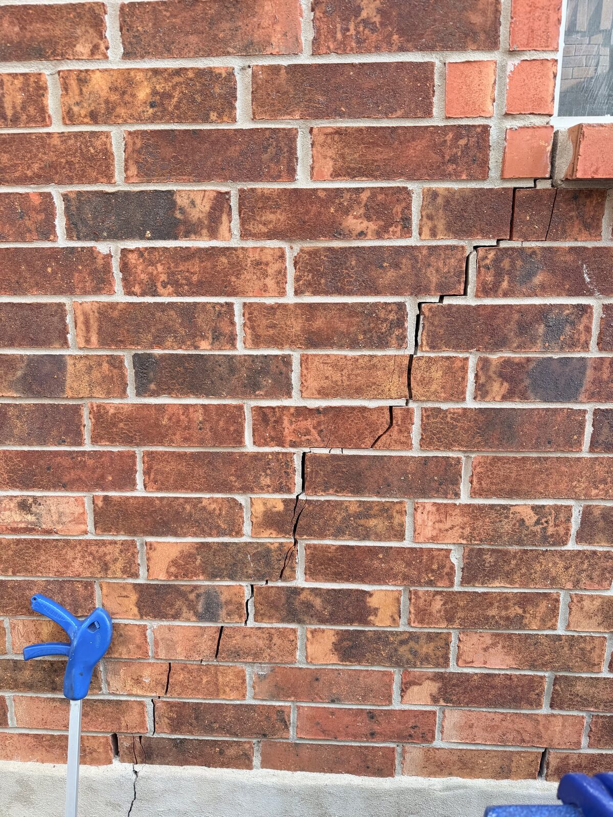 Stair-step crack in red brick running from a window corner down to the slab