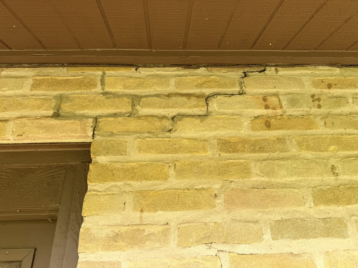 Stair-step crack in brick at a wall corner above a doorway, where foundation movement has opened the mortar joints