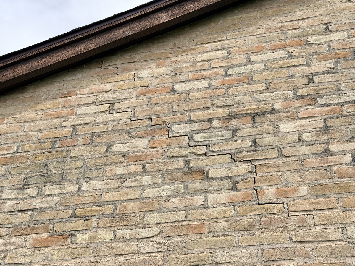 Stair-step crack climbing a brick gable toward the roofline
