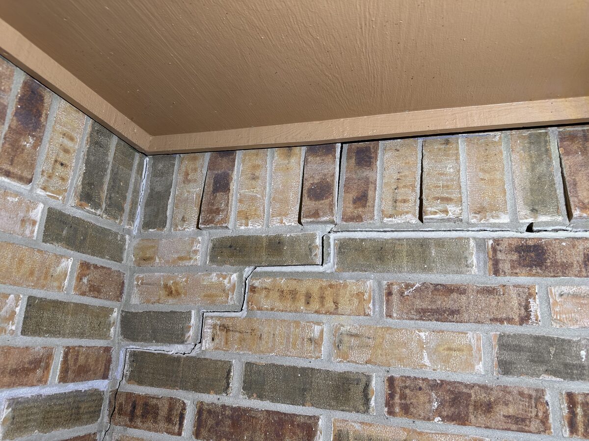 Stair-step crack and separation gap between brick veneer and the porch soffit, evidence of foundation settlement