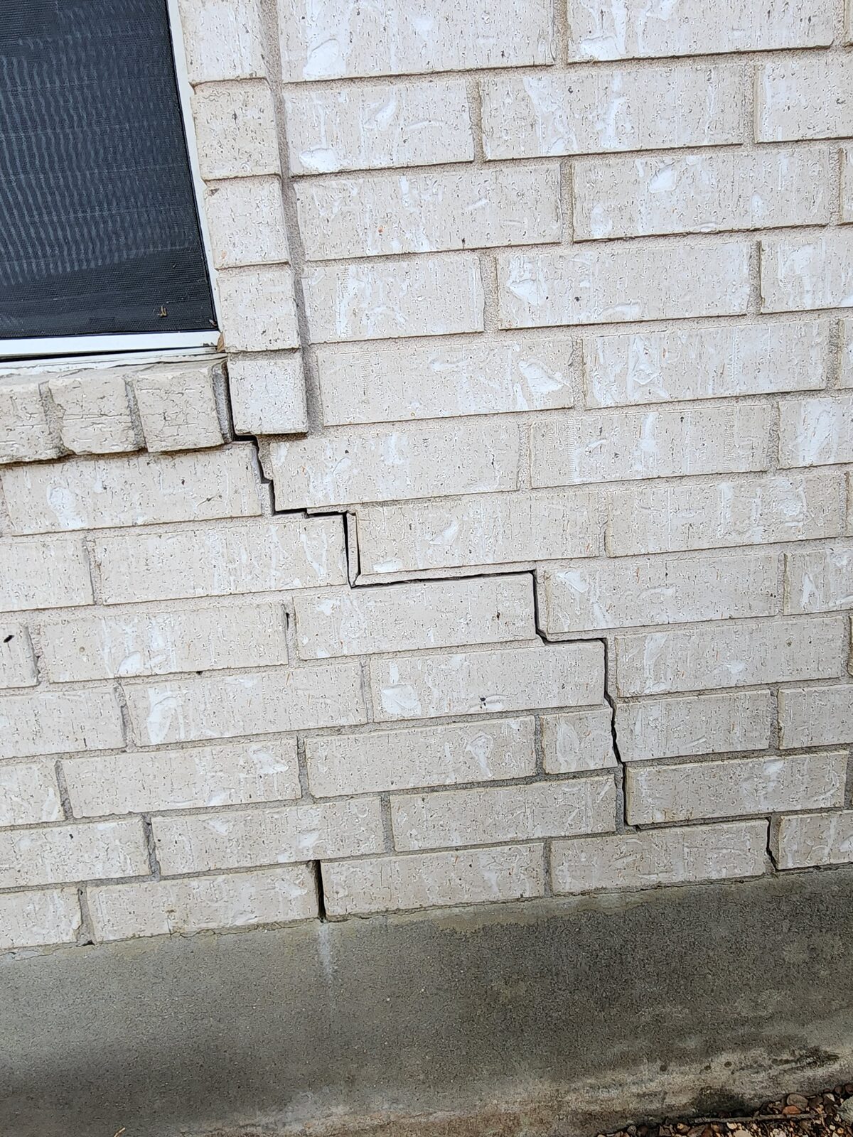 Stair-step crack through brick veneer mortar joints below a window, a hallmark of foundation settlement