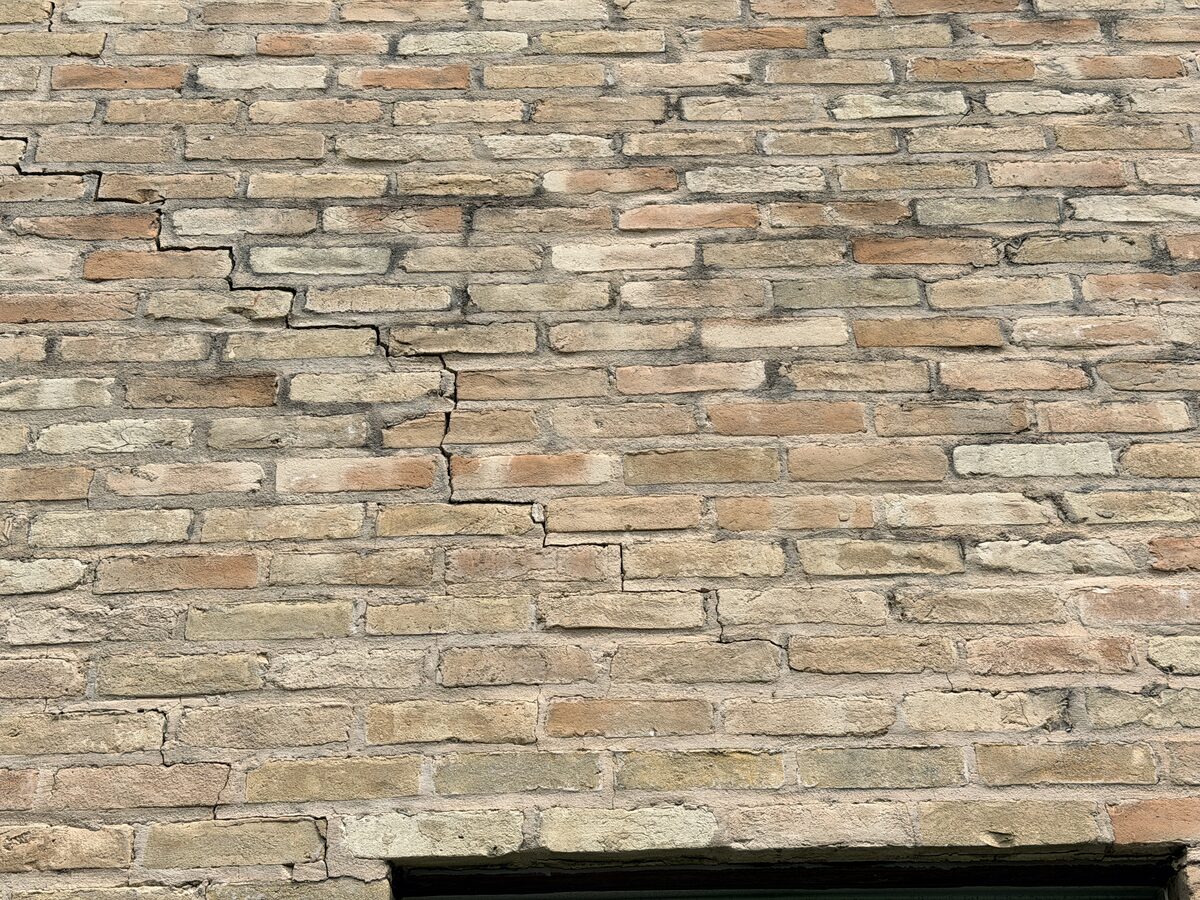 Prominent stair-step crack running through brick coursing near a wall opening on a settling house