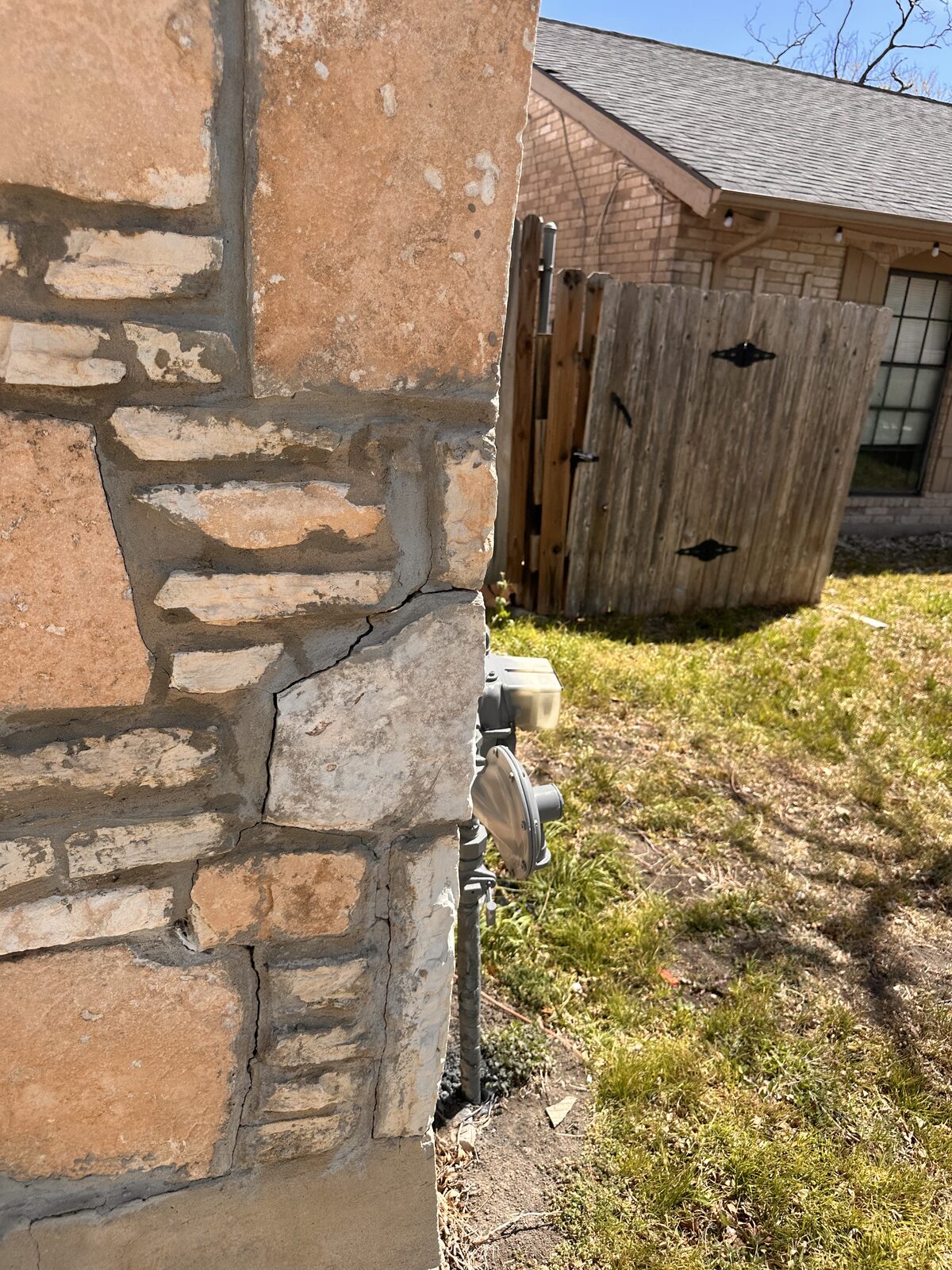 Stair-step crack in limestone veneer at a home's corner near the gas meter, a common sign of foundation settlement