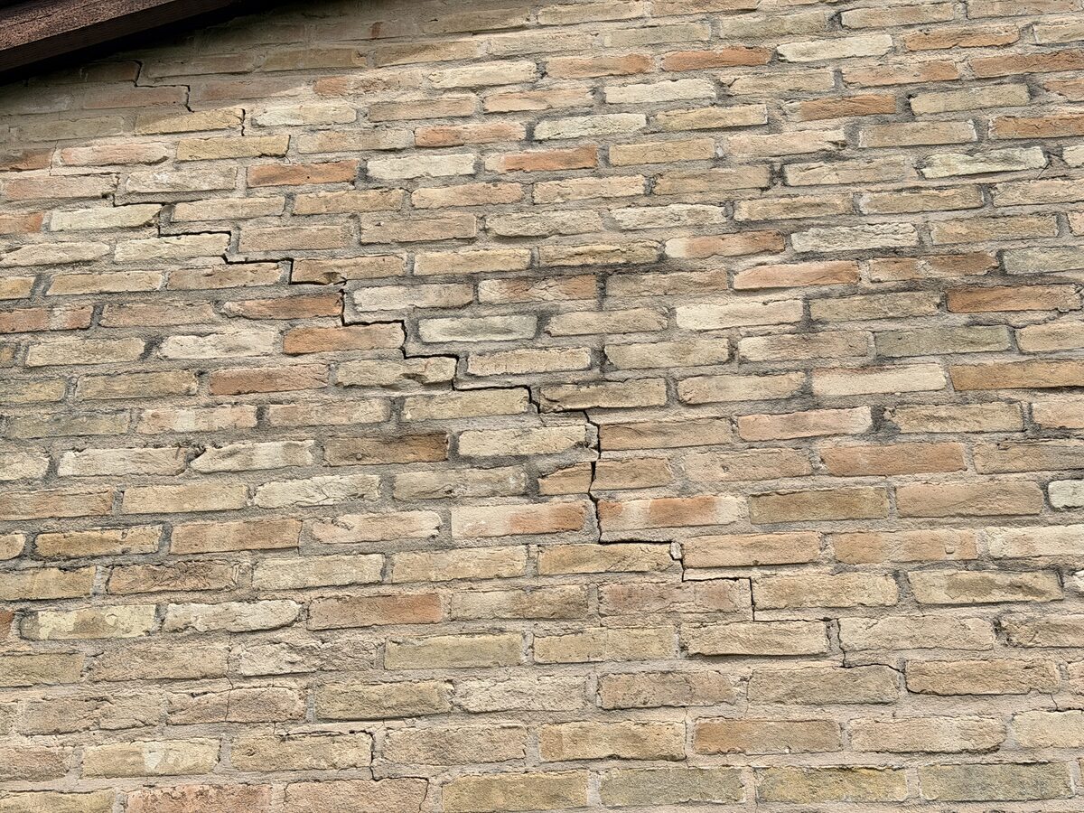 Extensive stair-step cracking across a brick gable end beneath the roofline, severe foundation settlement damage