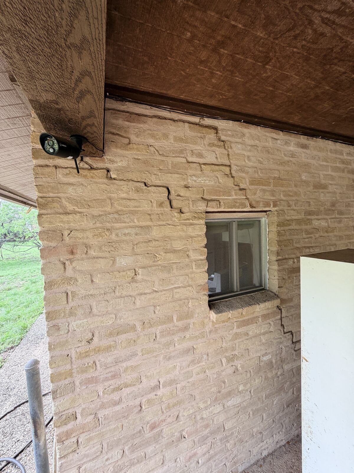 Stair-step crack in brick spreading from a porch ceiling corner toward a window, caused by foundation movement