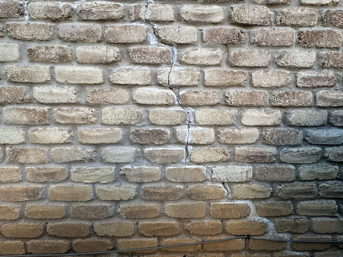 Stair-step crack descending through a tan brick wall, a classic exterior symptom of foundation settlement